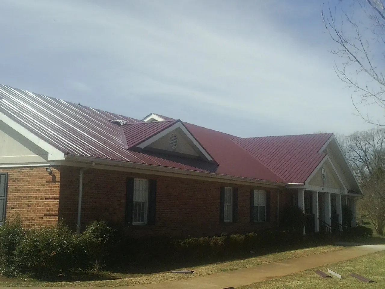 Red metal roof with gabled entries on a long brick building, from a Hail Damage Roof Repair job in Pensacola