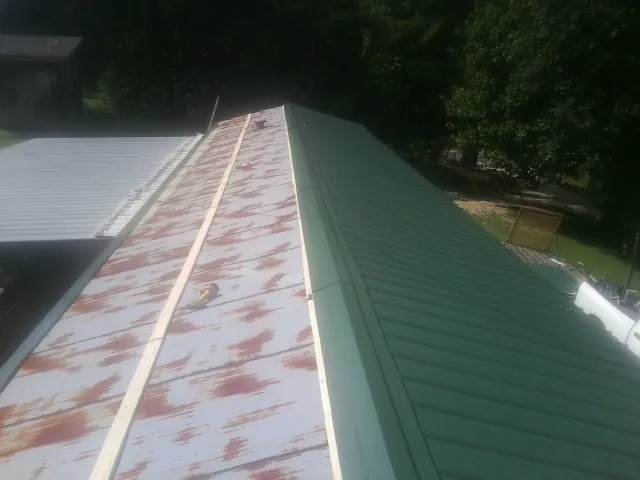 Old rusted panels beside newly installed green metal roofing — Wind Damage Roof Repair by Roofing Brothers in Pensacola