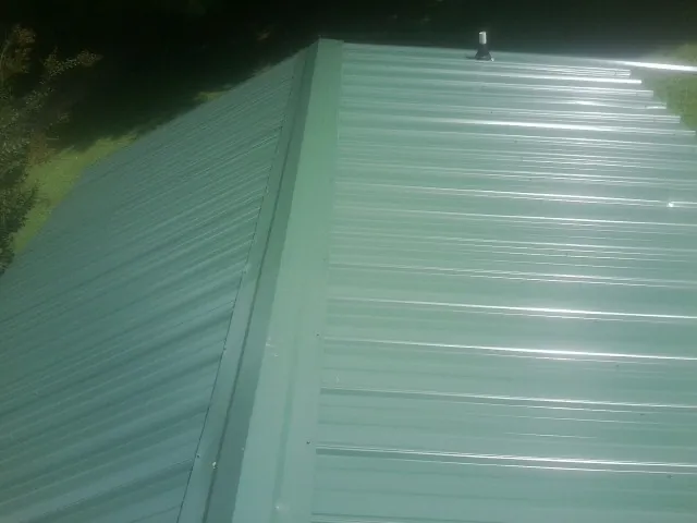 New green metal panels meeting at the ridge of a roof — Flat Roof Repair work by our crew in Pensacola