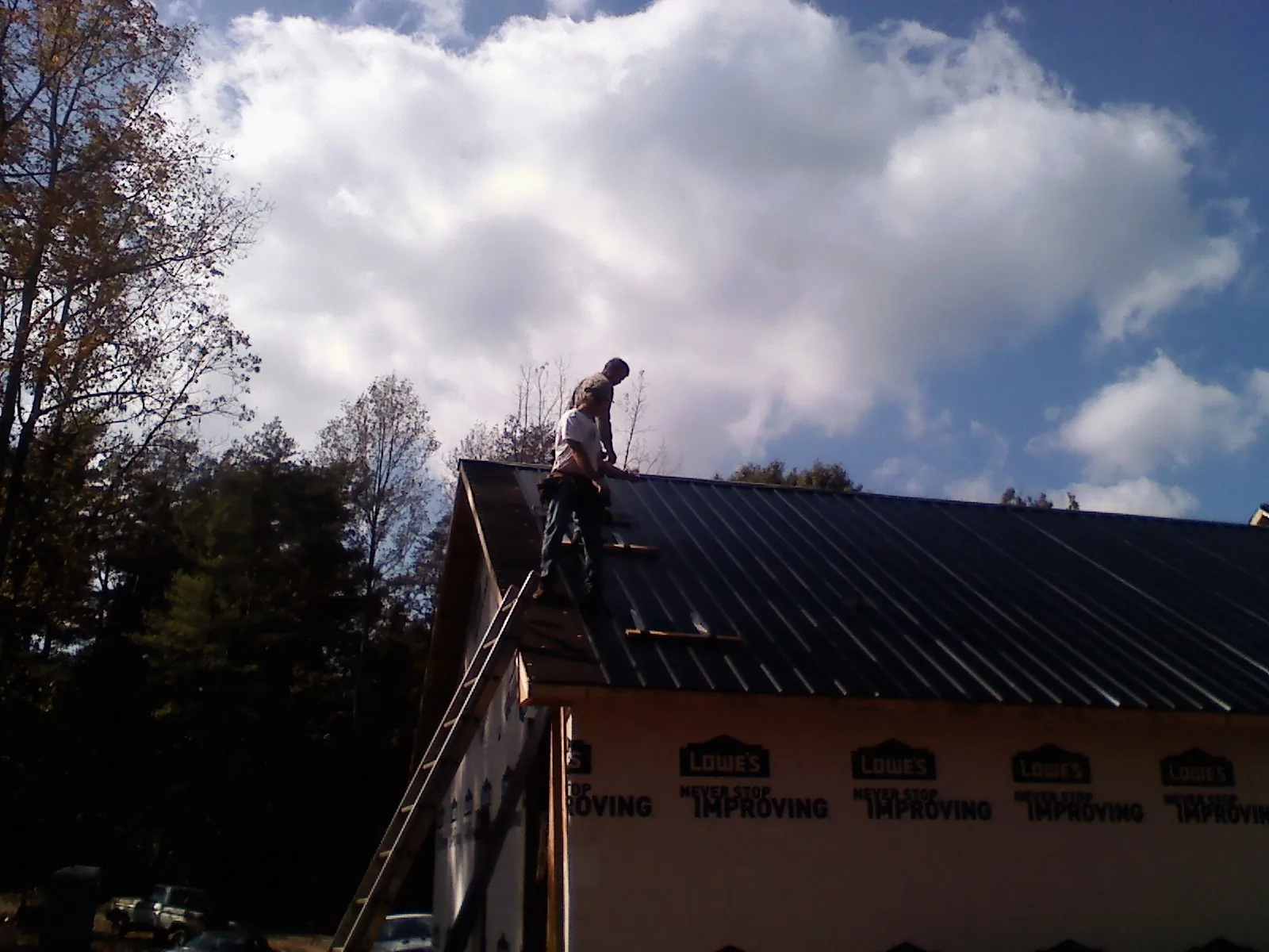Roofer fastening dark metal panels high against a cloudy sky, from a Roof Inspection job in Pensacola