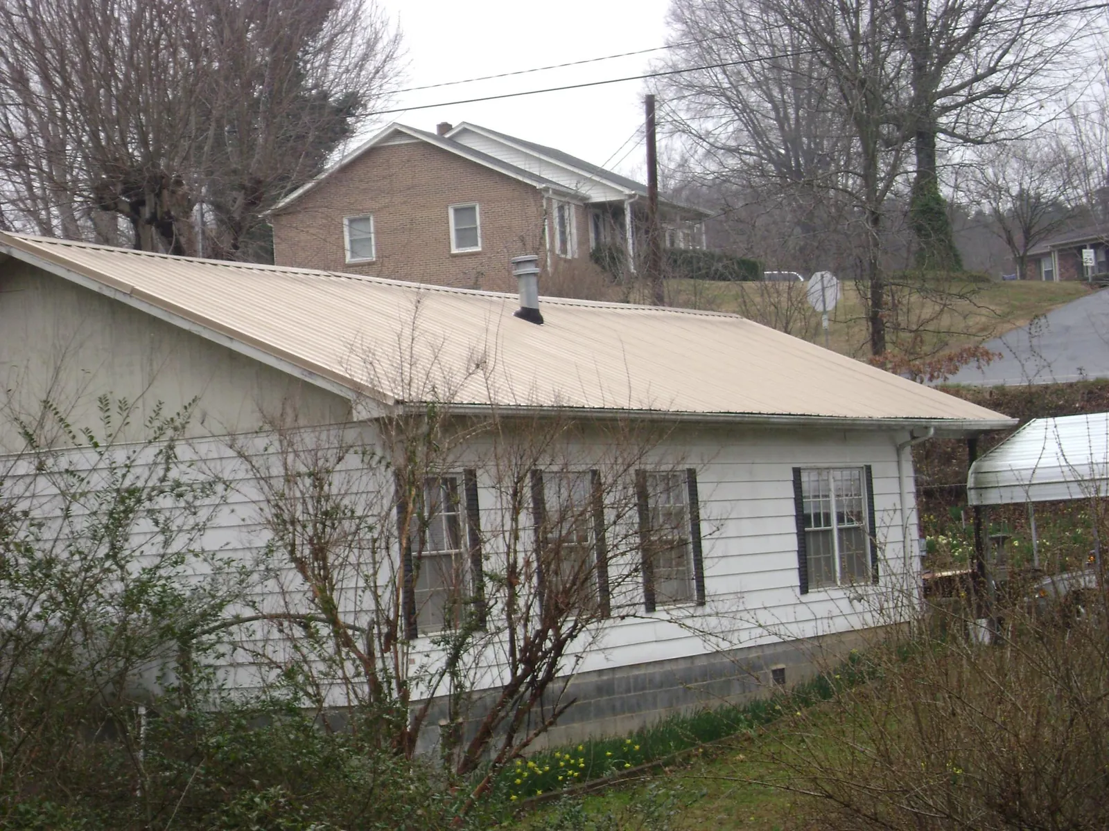Tan metal roof on a white sided house set into a hillside — Commercial Roofing by Roofing Brothers in Pensacola