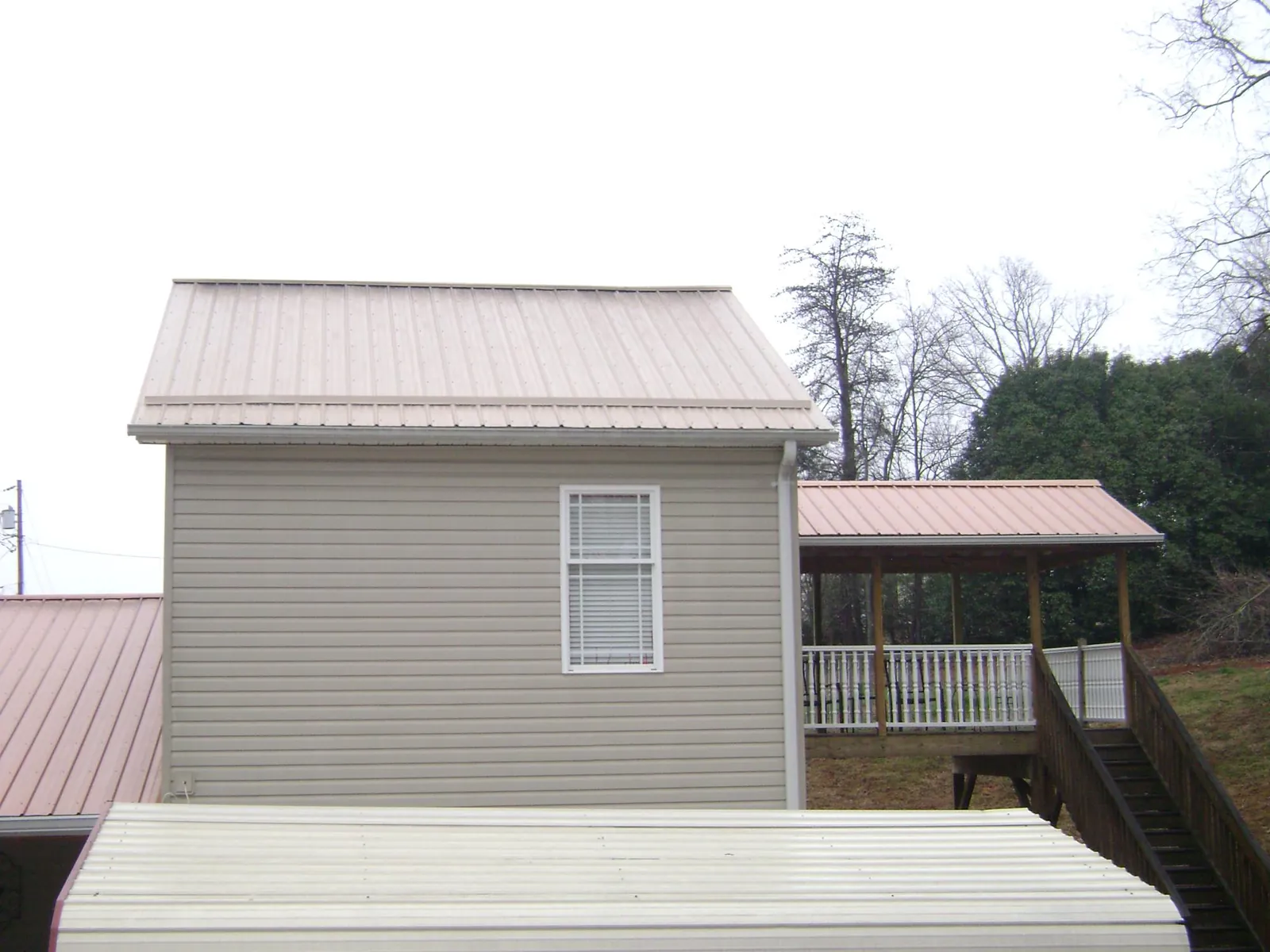 Tan metal roofs on a two story addition and attached porch, from a Roof Replacement job in Pensacola